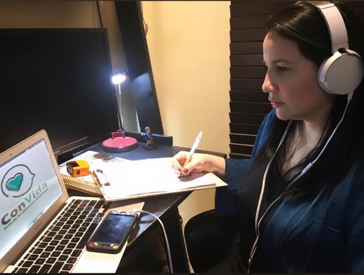 psicóloga usando fones de ouvido, sentada em frente a computador e segurando caneta sobre caderno
